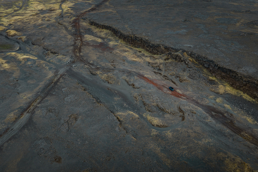 Aerial view of the rugged volcanic landscape near Sandfellshaed Viewpoint with a single vehicle driving on a dirt track through the dark lava fields in Keflavik Reykjanesbaer Iceland.