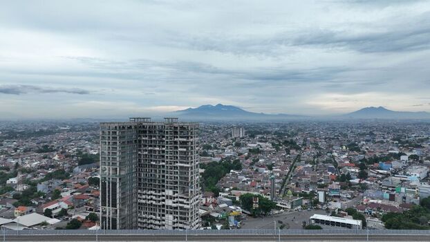 Aerial view of an unfinished high rise building surrounded by dense urban sprawl and residential rooftops under a cloudy sky in Bekasi Barat West Java Indonesia.