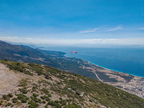Aerial view of Bregdet.al Llogara Pass with a paraglider soaring above the rugged mountain slopes and the turquoise Ionian Sea coastline in Llogara Vlore County Albania. Aerial view of Bregdet.al Llogara Pass with a paraglider soaring above the rugged mountain slopes and the turquoise Ionian Sea coastline in Llogara Vlore County Albania.