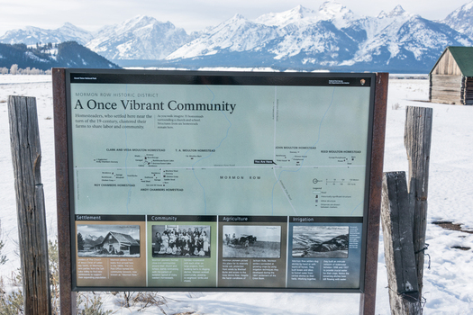 View of an information sign at the Mormon Row Historic District with snow capped Teton mountains in the background in Teton County Wyoming United States.