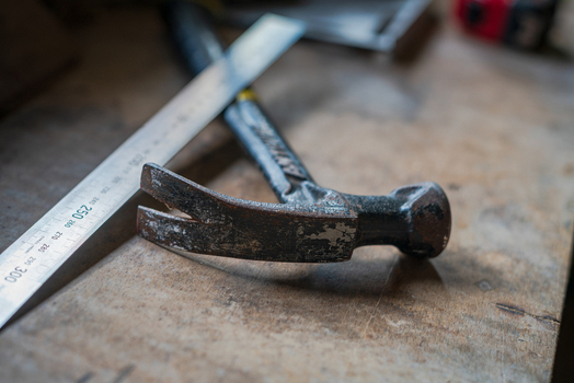 View of a weathered claw hammer and a metal ruler resting on a rustic wooden workbench in Looe Cornwall United Kingdom. View of a weathered claw hammer and a metal ruler resting on a rustic wooden workbench in Looe Cornwall United Kingdom.