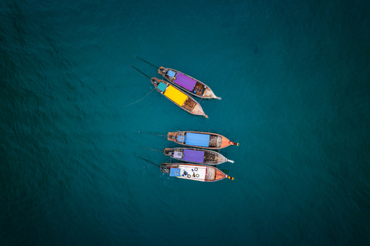 Aerial view of long tail boats with colorful roofs floating on the clear turquoise water near Railay Beach in Ao Nang Krabi Thailand. Aerial view of long tail boats with colorful roofs floating on the clear turquoise water near Railay Beach in Ao Nang Krabi Thailand.