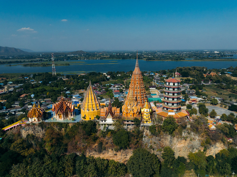 Aerial view of Wat Tham Suea temple complex with its iconic golden stupas and pagodas perched on a rocky hill overlooking the Mae Klong River under a clear blue sky Muang Chum Kanchanaburi Thailand. Aerial view of Wat Tham Suea temple complex with its iconic golden stupas and pagodas perched on a rocky hill overlooking the Mae Klong River under a clear blue sky Muang Chum Kanchanaburi Thailand.