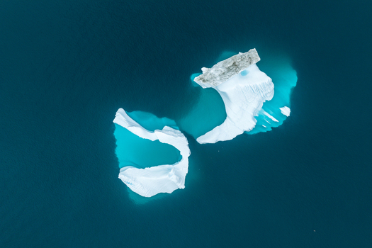 Aerial view of two icebergs floating in deep blue water in Greenland.