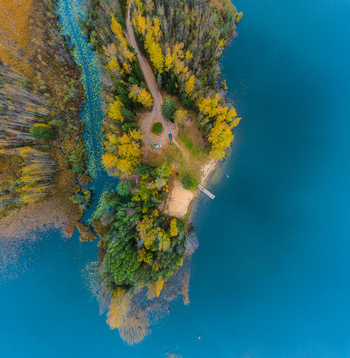 Aerial view of a peninsula with vibrant autumn foliage a dirt road leading to a small parking area and a wooden pier extending into the blue lake in Cesis Cesis Municipality Latvia. Aerial view of a peninsula with vibrant autumn foliage a dirt road leading to a small parking area and a wooden pier extending into the blue lake in Cesis Cesis Municipality Latvia.