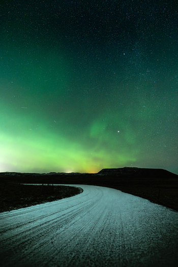 View of the winding road under the vibrant green and blue aurora borealis lights dancing across the starry night sky Krysuvikurkirkja Hafnarfjardarkaupstadur Iceland.