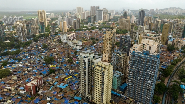 Aerial view of the dense Dharavi Slums with a mix of informal housing and modern high rise buildings in the background in Mumbai Maharashtra India. Aerial view of the dense Dharavi Slums with a mix of informal housing and modern high rise buildings in the background in Mumbai Maharashtra India.