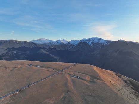 Aerial view of the Sibillini Mountains with snow capped peaks and a winding road traversing the grassy slopes in Montemonaco Marche Italy.