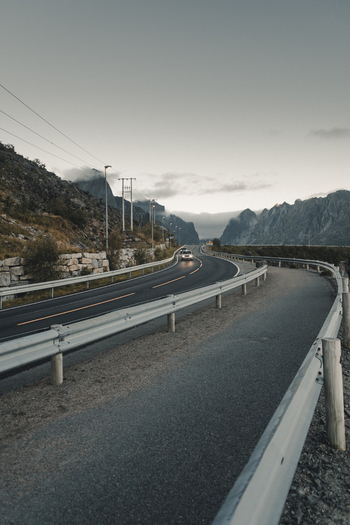 View of the winding road near Reinebringen with rugged mountains and guardrails under a cloudy sky in Moskenes Nordland Norway.