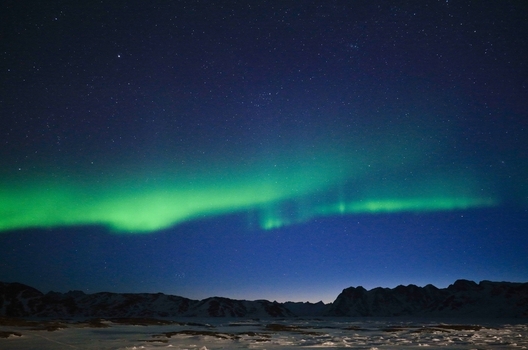 Aerial view of the vibrant green Aurora Borealis dancing across a starry night sky over snow covered mountains in Tasiilaq Sermersooq Municipality Greenland. Aerial view of the vibrant green Aurora Borealis dancing across a starry night sky over snow covered mountains in Tasiilaq Sermersooq Municipality Greenland.