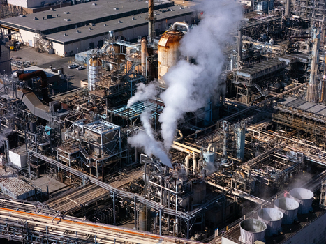 Aerial view of an industrial oil refinery with complex piping networks metal storage tanks and cooling towers emitting steam in Carson California United States.