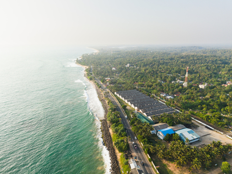 Aerial view of a tropical coastline with turquoise waves crashing against the shore a coastal road and lush green vegetation in Galle Southern Province Sri Lanka.