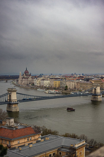 View of the Széchenyi Chain Bridge stretching across the Danube River under a brooding sky with ornate buildings lining the waterfront Budapest Hungary. View of the Széchenyi Chain Bridge stretching across the Danube River under a brooding sky with ornate buildings lining the waterfront Budapest Hungary.