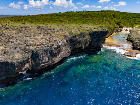 Aerial view of Chigit Beach featuring rugged limestone cliffs turquoise coastal waters and lush green vegetation in Northern Tinian Tinian Northern Mariana Islands. Aerial view of Chigit Beach featuring rugged limestone cliffs turquoise coastal waters and lush green vegetation in Northern Tinian Tinian Northern Mariana Islands.