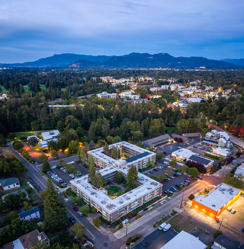 Aerial view of a residential complex with a central courtyard surrounded by lush trees parking areas and urban infrastructure in Eugene Oregon United States. Aerial view of a residential complex with a central courtyard surrounded by lush trees parking areas and urban infrastructure in Eugene Oregon United States.