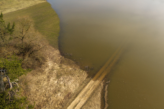 Aerial view of a flooded dirt road disappearing into murky water near a grassy shoreline and trees in Kaniukai Kaunas County Lithuania. Aerial view of a flooded dirt road disappearing into murky water near a grassy shoreline and trees in Kaniukai Kaunas County Lithuania.