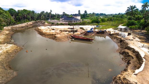 Aerial view of the Bukuma creek featuring small wooden boats moored on muddy banks surrounded by lush palm trees and a building in Buguma Rivers Nigeria.