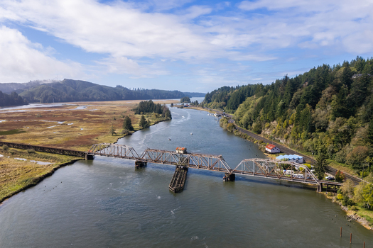 Aerial view of the Siuslaw River near Florence Oregon with salmon fishing boats the Coos Bay Rail Line bridge wetlands forest and a scenic Oregon Coast landscape.