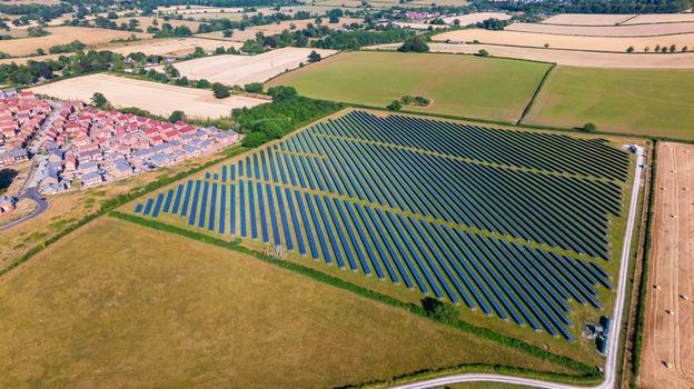 Aerial view of a large solar farm with rows of photovoltaic panels situated next to a residential neighborhood and agricultural fields in Dorset England United Kingdom. Aerial view of a large solar farm with rows of photovoltaic panels situated next to a residential neighborhood and agricultural fields in Dorset England United Kingdom.