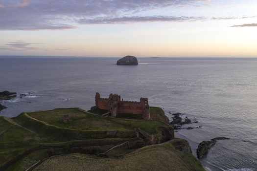 Aerial view of Tantallon Castle ruins on the edge of a cliff overlooking the North Sea and Bass Rock under a soft twilight sky North Berwick Scotland United Kingdom.