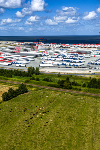 Aerial view of the Siemens Gamesa Renewable Energy facility with wind turbine blades stored in an industrial yard near the coast with grazing cows in Cuxhaven Niedersachsen Germany.