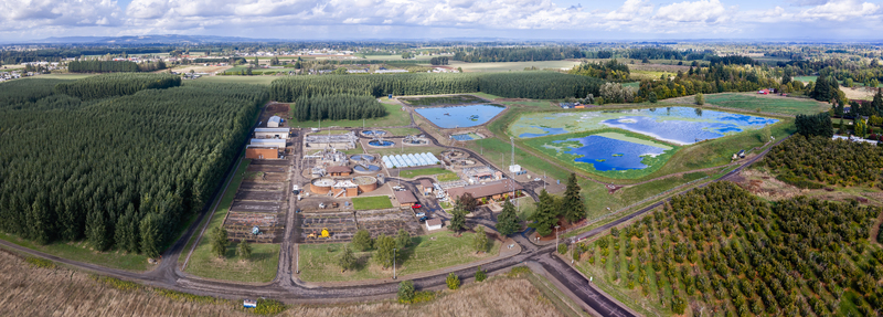 Aerial view of wastewater treatment plant with circular tanks filtration ponds and surrounding agricultural fields and forests in Woodburn Oregon United States. Aerial view of wastewater treatment plant with circular tanks filtration ponds and surrounding agricultural fields and forests in Woodburn Oregon United States.