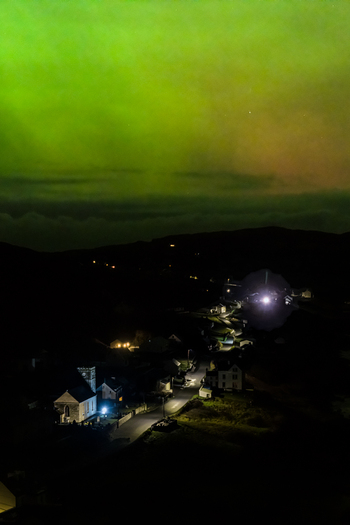 Aerial view of Aurora Borealis illuminating the night sky above the quiet village of Portnoo with illuminated houses and winding roads in Portnoo County Donegal Ireland.