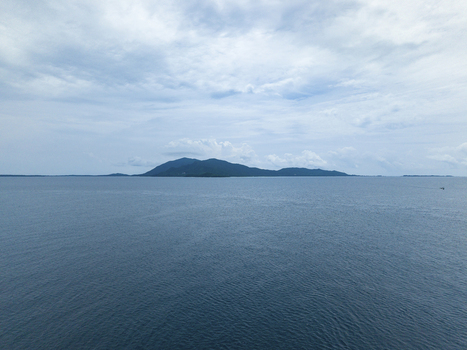 Aerial view of the shimmering ocean stretching to the horizon under a cloudy sky with a distant island silhouette Karimunjawa Central Java Indonesia.
