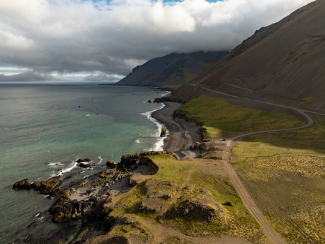 Aerial view of Stapavik coastline featuring rugged cliffs a black sand beach and a winding road along the mountain slopes in Njardhvik Mulathing Iceland. Aerial view of Stapavik coastline featuring rugged cliffs a black sand beach and a winding road along the mountain slopes in Njardhvik Mulathing Iceland.
