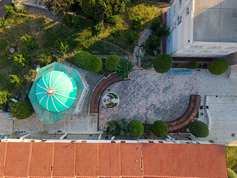 Aerial view of a building with a bright turquoise dome and a paved courtyard with curved benches and manicured trees in Kruje Durres County Albania.