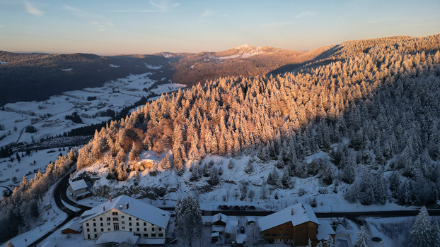 Aerial view of Col de la Faucille featuring snow covered pine forests and mountain buildings illuminated by the warm light of the setting sun in Gex Auvergne Rhone Alpes France. Aerial view of Col de la Faucille featuring snow covered pine forests and mountain buildings illuminated by the warm light of the setting sun in Gex Auvergne Rhone Alpes France.