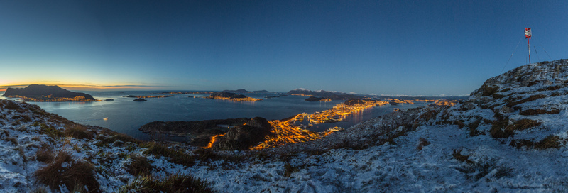 Aerial view of the city of Alesund at twilight with snow covered mountain slopes in the foreground and illuminated city streets reflecting on the water in Alesund More og Romsdal Norway. Aerial view of the city of Alesund at twilight with snow covered mountain slopes in the foreground and illuminated city streets reflecting on the water in Alesund More og Romsdal Norway.