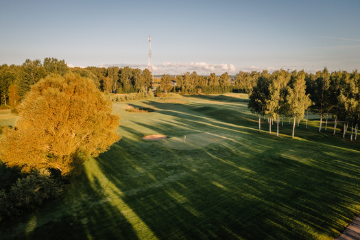 Aerial view of a lush green golf course with sand bunkers and long tree shadows during golden hour in Valmiera Valmiera Latvija.