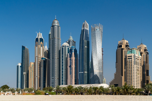 View of the modern Dubai Marina skyline featuring the twisted Cayan Tower and high rise skyscrapers under a clear blue sky from the beach in Dubai Dubai United Arab Emirates. View of the modern Dubai Marina skyline featuring the twisted Cayan Tower and high rise skyscrapers under a clear blue sky from the beach in Dubai Dubai United Arab Emirates.
