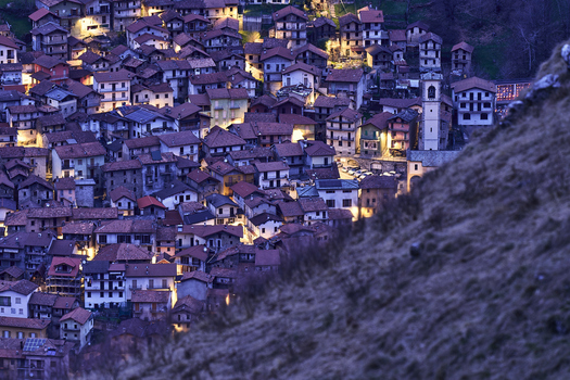 View of the historic village of Monti del lago di Como nestled in the mountains with illuminated stone houses and narrow streets at twilight in Lombardia Italy. View of the historic village of Monti del lago di Como nestled in the mountains with illuminated stone houses and narrow streets at twilight in Lombardia Italy.