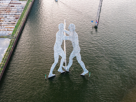 Aerial view of the Molecule Men sculpture standing in the Spree river with calm water and a nearby pier in Berlin Berlin Germany. Aerial view of the Molecule Men sculpture standing in the Spree river with calm water and a nearby pier in Berlin Berlin Germany.
