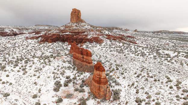 Aerial view of red sandstone buttes and rock formations covered in a light layer of snow under an overcast sky in Page Arizona United States.