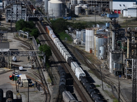 Aerial view of a long freight train moving through an industrial refinery complex with storage tanks and railway infrastructure in Cincinnati OH United States. Aerial view of a long freight train moving through an industrial refinery complex with storage tanks and railway infrastructure in Cincinnati OH United States.