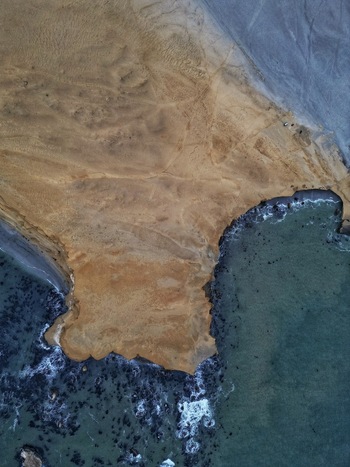 Aerial view of the rugged desert coastline of Reserva Nacional de Paracas with golden cliffs meeting the turquoise ocean waves Paracas Ica Peru.