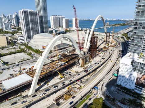 Aerial view of the construction of the dramatic arch of the signature bridge over I 95 a symphony of steel and concrete amidst the vibrant cityscape and bay waters Miami Florida USA. Aerial view of the construction of the dramatic arch of the signature bridge over I 95 a symphony of steel and concrete amidst the vibrant cityscape and bay waters Miami Florida USA.