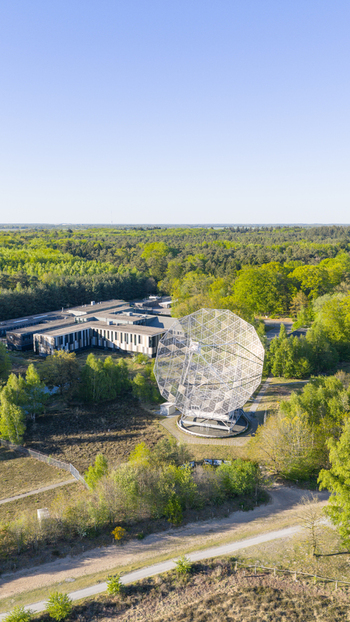 Aerial view of the Radiotelescoop surrounded by dense green forest and research buildings under a clear blue sky in Dwingeloo Drenthe Netherlands.