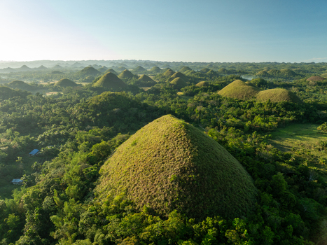 Aerial view of the Chocolate Hills a series of unique conical limestone hills covered in lush green grass and tropical vegetation in Batuan Central Visayas Philippines. Aerial view of the Chocolate Hills a series of unique conical limestone hills covered in lush green grass and tropical vegetation in Batuan Central Visayas Philippines.
