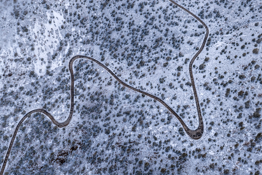 Aerial view of a winding road snaking through the snow covered slopes of the White Mountains with scattered pine trees in Mono County California United States.