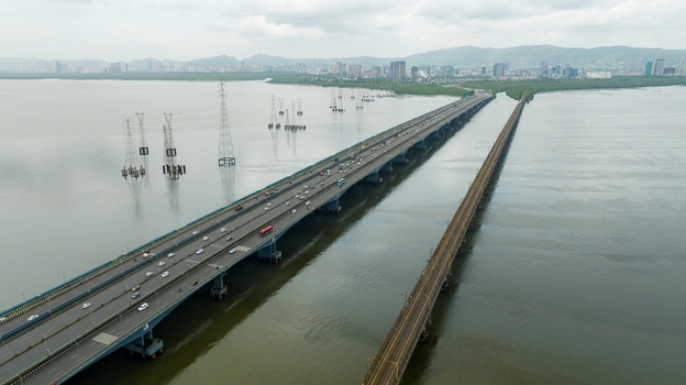 Aerial view of Vashi bridge spanning the creek with road and rail traffic power pylons in the water and the city skyline in the background in Navi Mumbai Maharashtra India.