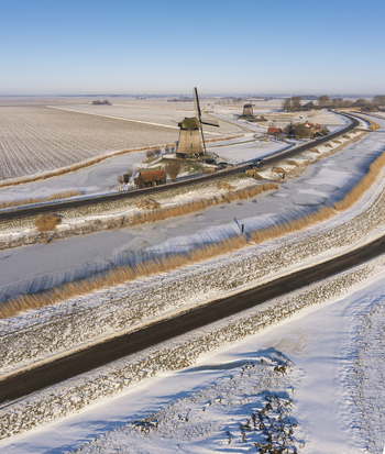Aerial view of a traditional Dutch windmill surrounded by snow covered fields and frozen canals in Ursem North Holland Netherlands. Aerial view of a traditional Dutch windmill surrounded by snow covered fields and frozen canals in Ursem North Holland Netherlands.
