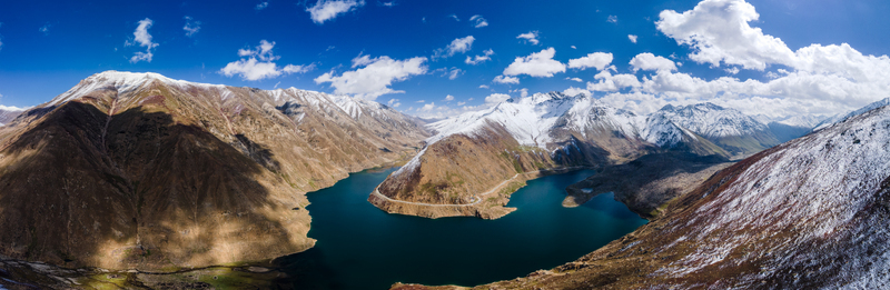 Aerial view of Lulusar Lake surrounded by snow capped mountain peaks and rugged terrain under a bright blue sky with white clouds in Balakot Khyber Pakhtunkhwa Pakistan. Aerial view of Lulusar Lake surrounded by snow capped mountain peaks and rugged terrain under a bright blue sky with white clouds in Balakot Khyber Pakhtunkhwa Pakistan.