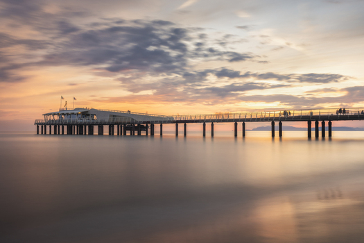 View of the modern pier extending into the calm sea under a soft sunset sky with silhouettes of people Lido di Camaiore Tuscany Italy.