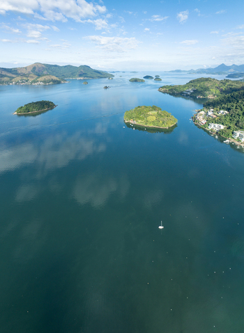 Aerial view of the islands and coastal waters with lush green hills calm blue sea and a small sailboat in Angra dos Reis Rio de Janeiro Brazil.