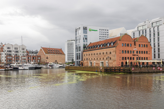Gdansk Poland 05 September 2026 View of the Motlawa River waterfront with historic brick granary buildings modern hotels and boats docked along the quay under a cloudy sky. Gdansk Poland 05 September 2026 View of the Motlawa River waterfront with historic brick granary buildings modern hotels and boats docked along the quay under a cloudy sky.