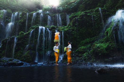 Bali Indonesia View of women in traditional Balinese dress amidst the cascading Banyu Wana Amertha waterfalls a symphony of emerald moss and silver streams. Bali Indonesia View of women in traditional Balinese dress amidst the cascading Banyu Wana Amertha waterfalls a symphony of emerald moss and silver streams.
